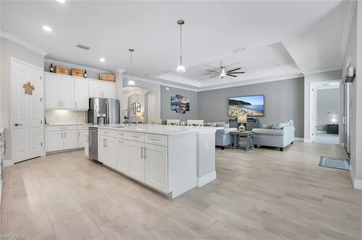 Kitchen with arched walkways, hanging light fixtures, a ceiling fan, ornamental molding, and white cabinets
