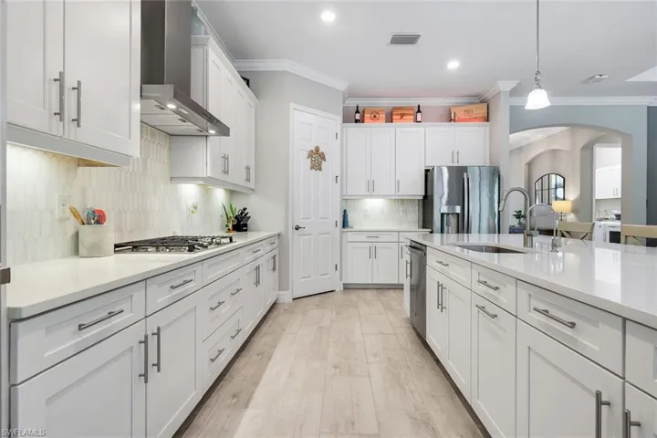 Kitchen with arched walkways, wall chimney exhaust hood, backsplash, stainless steel appliances, and white cabinets