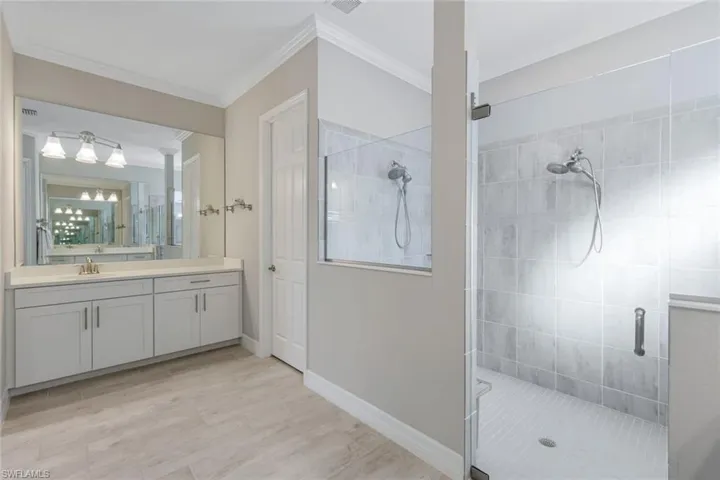 Bathroom featuring vanity, walk in shower, ornamental molding, and light wood finished floors