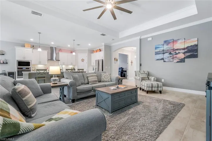 Living room with crown molding, a raised ceiling, light tile patterned floors, arched walkways, and beverage cooler