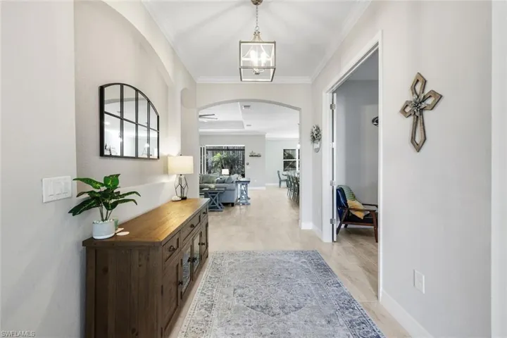 Hallway featuring arched walkways, ornamental molding, light wood finished floors, and a chandelier