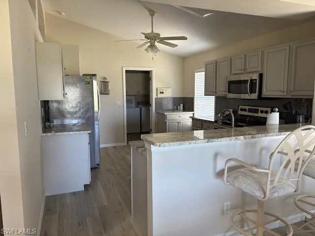 Kitchen featuring ceiling fan, a peninsula, vaulted ceiling, stainless steel appliances, and washing machine and dryer