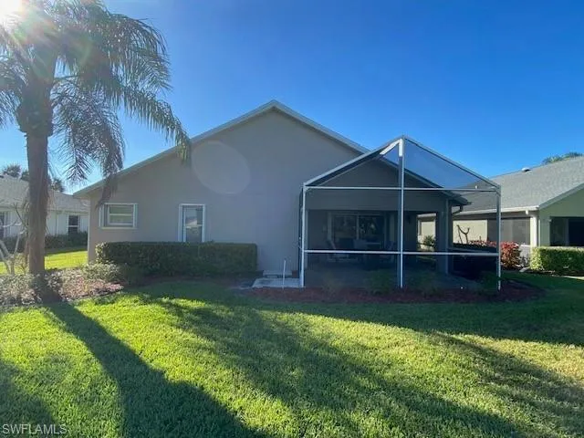 Back of property featuring a lawn and screened in lanai
