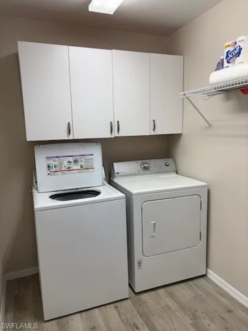 Laundry room with light wood-style floors, separate washer and dryer, baseboards, and cabinet space