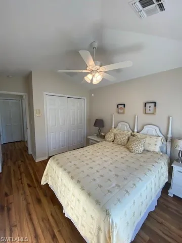 Bedroom with a closet, ceiling fan, dark vinyl / wood-style flooring, and lofted ceiling