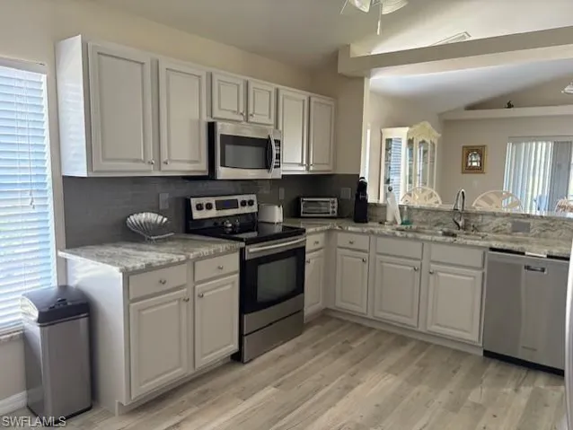 Kitchen featuring tasteful backsplash, a sink, white cabinetry, stainless steel appliances, and light wood-style flooring