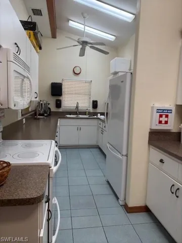 Kitchen with sink, vaulted ceiling with beams, light tile patterned flooring, stove with oven and refrigerator, and white cabinets