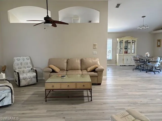 Living room featuring arched walkways, visible vents, ceiling fan with notable chandelier, and light wood-style flooring
