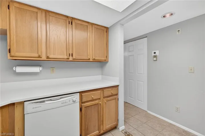 Kitchen featuring dishwasher, light countertops, light tile patterned floors, a skylight, and light brown cabinetry