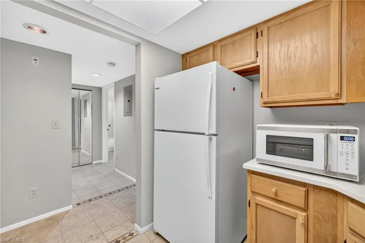 Kitchen with white appliances, light countertops, light tile patterned flooring, light brown cabinets, and electric panel