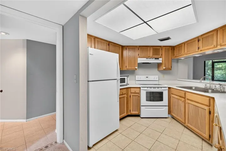 Kitchen with light tile patterned flooring, white appliances, light countertops, and under cabinet range hood
