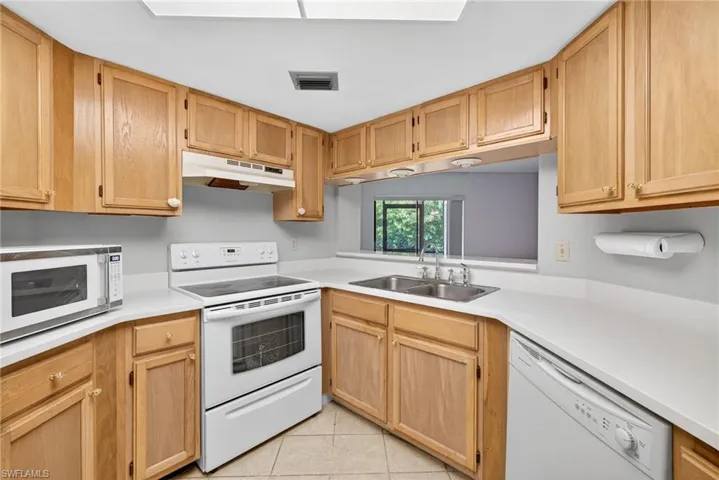 Kitchen with white appliances, light countertops, under cabinet range hood, and light tile patterned floors