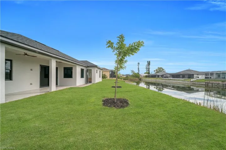 View of green lawn featuring a ceiling fan, a patio area, a water view, and a residential view