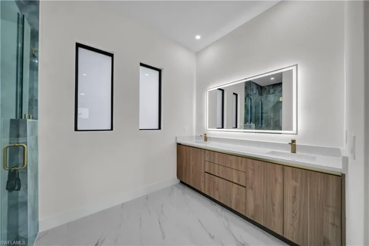 Full bathroom featuring a marble finish shower, light marble finish flooring, double vanity, and recessed lighting