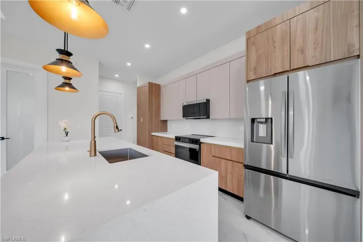 Kitchen featuring appliances with stainless steel finishes, pendant lighting, light stone counters, modern cabinets, and recessed lighting