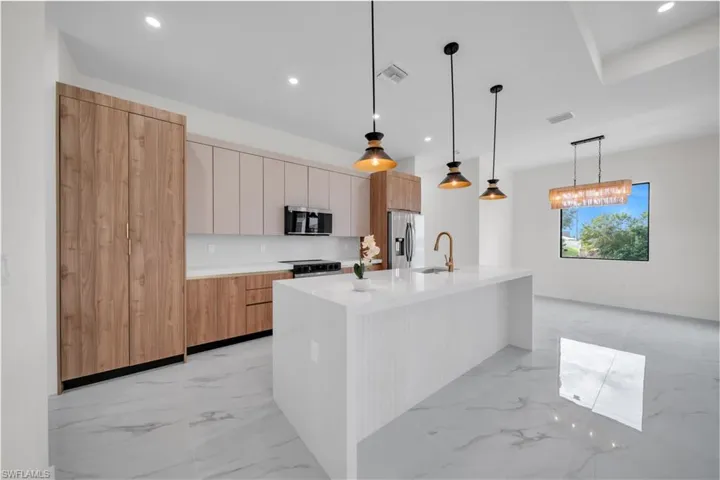 Kitchen with modern cabinets, light marble finish flooring, an island with sink, hanging light fixtures, and recessed lighting