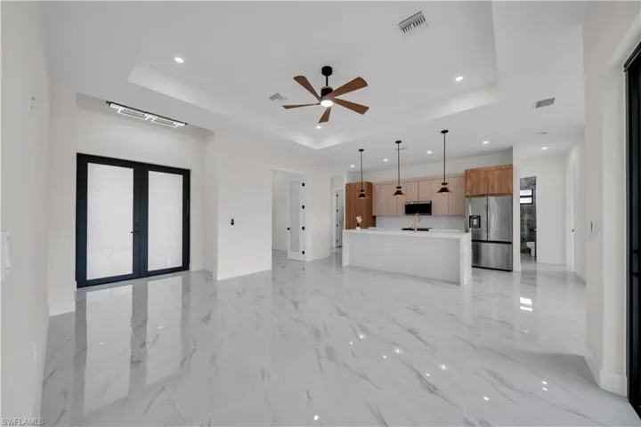 Unfurnished living room featuring a tray ceiling, recessed lighting, french doors, ceiling fan, and light marble finish flooring
