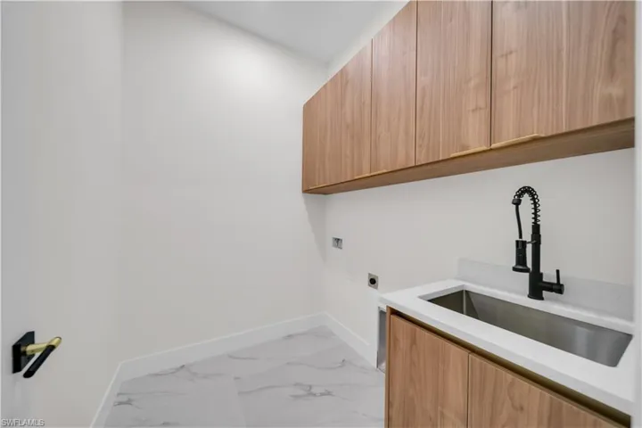 Laundry room featuring light marble finish flooring, electric dryer hookup, and cabinet space