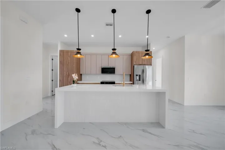 Kitchen featuring modern cabinets, an island with sink, hanging light fixtures, appliances with stainless steel finishes, and light stone counters