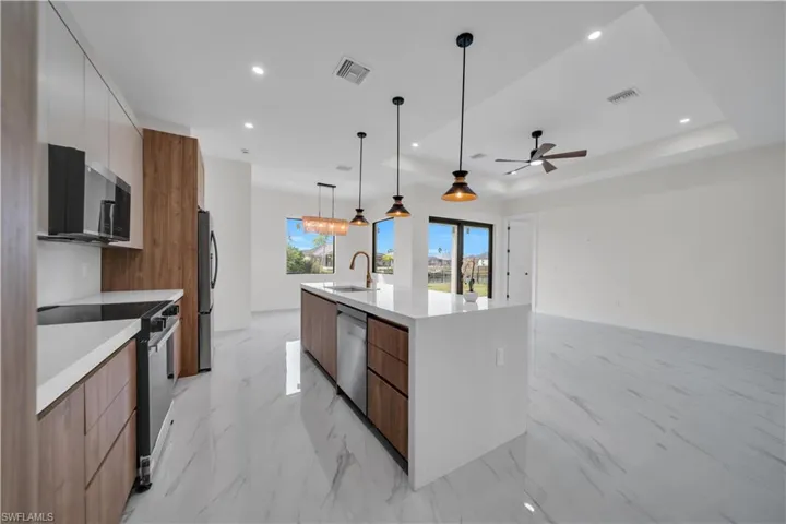 Kitchen with modern cabinets, brown cabinetry, stainless steel appliances, decorative light fixtures, and light stone countertops