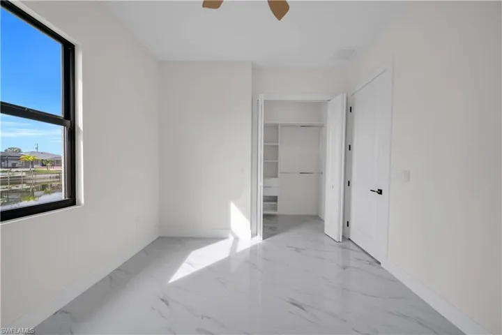 Unfurnished bedroom with light marble finish flooring, ceiling fan, and a walk in closet