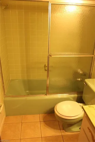 Full bathroom with shower / bath combination with glass door, vanity, tile patterned floors, and toilet