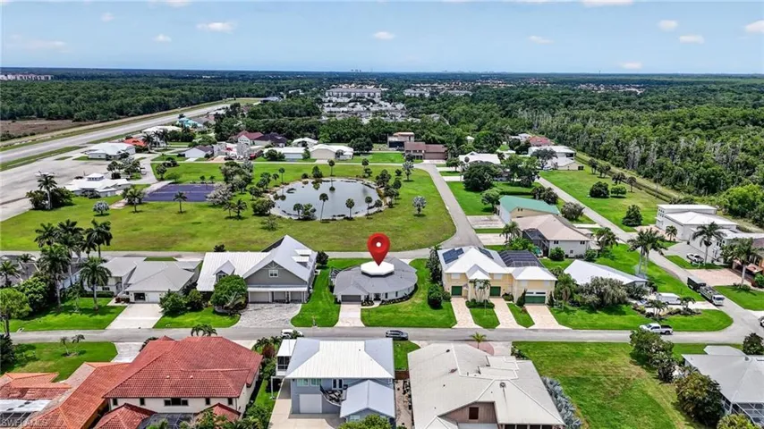 Circular residence with taxiway to the runway, a light gray exterior and white trim, featuring a paved driveway and surrounding manicured lawn