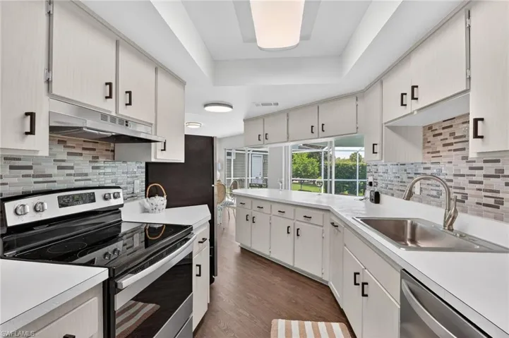 Kitchen featuring light cabinetry, a mosaic tile backsplash, a stainless steel sink, wood-finish flooring, and white countertops