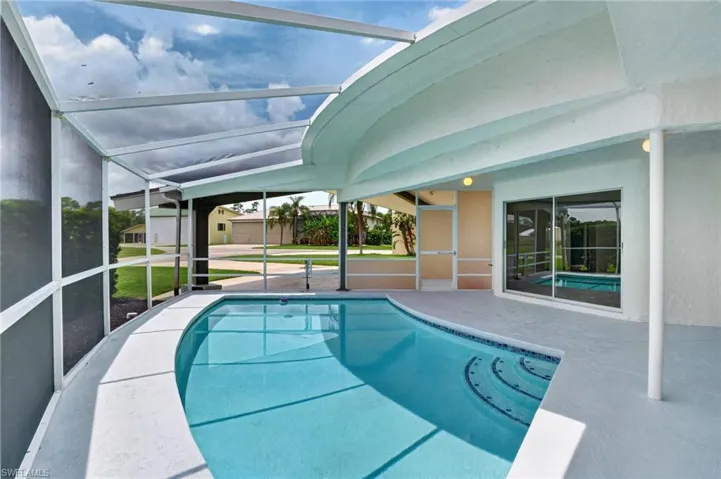 Screened pool enclosure featuring a curvilinear pool with tiled steps, a patio deck, and sliding glass door access is view from the living room, kitchen, and the dining area