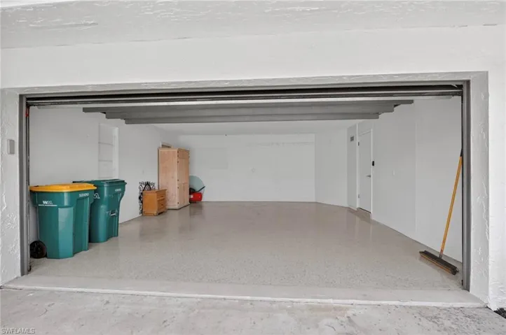 Spacious garage featuring a durable epoxy floor, white painted walls, and overhead structural beams