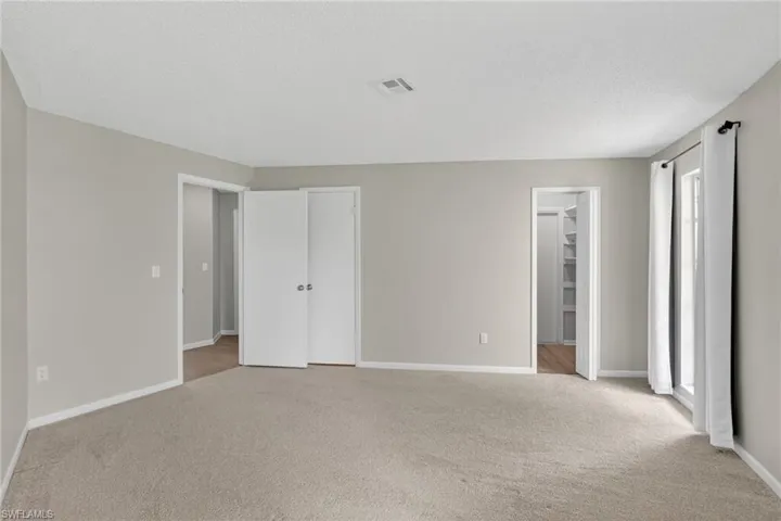 Carpeted interior room featuring light-toned walls, white trim, and a window with white curtains