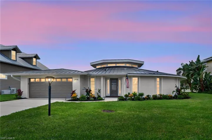 Circular modern home featuring a low-pitched metal roof, integrated garage, manicured lawn, and mature landscaping