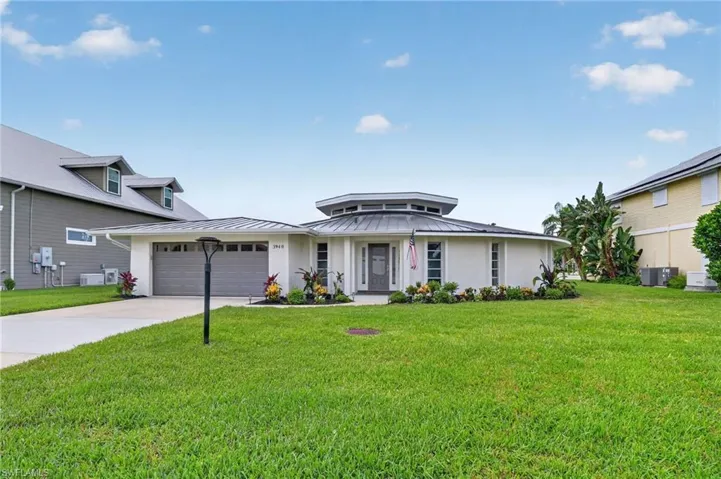 Distinctive circular architectural design featuring a multi-paneled front door, an attached two-car garage with a panel door, a paved driveway, and mature landscaping
