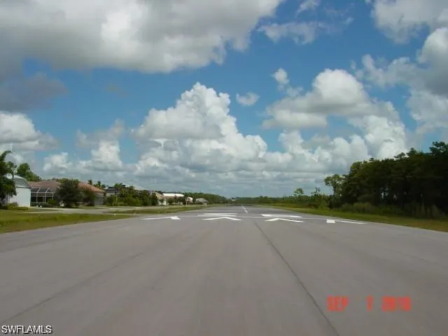 Paved asphalt runway with directional markings, bordered by green spaces and distant residential properties