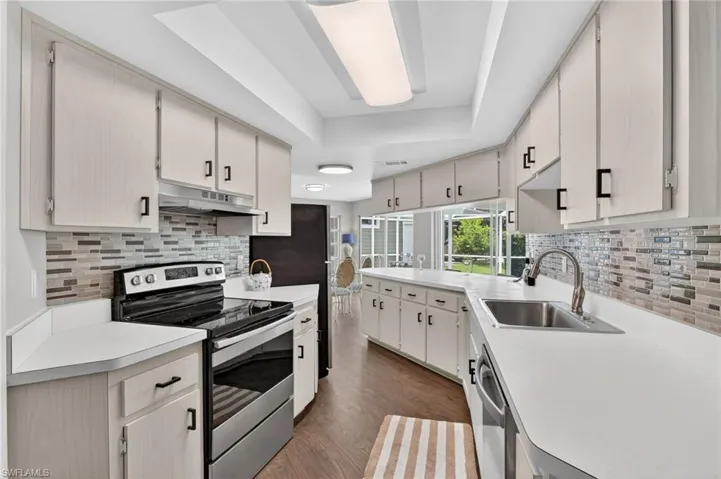 Kitchen featuring light cabinetry with black hardware, white countertops, stainless steel sink with gooseneck faucet, an attractive glass tile backsplash, and wood-finish flooring