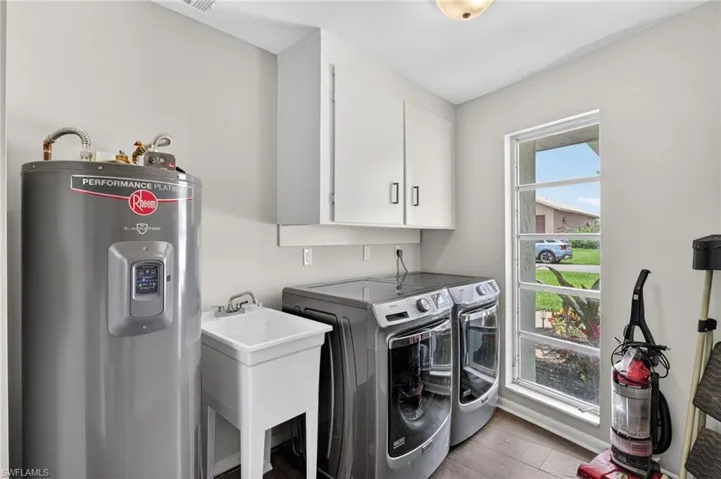 Dedicated laundry space featuring wood-finish flooring, white cabinetry, a utility sink, and a large window providing natural light