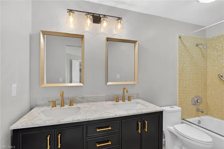 Bathroom featuring a dual vanity with a dark wood-finish cabinet, light-toned countertop, and gold-finish hardware