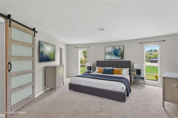Spacious room featuring light-colored carpeting, multiple windows, and a barn door with frosted glass panels to bathroom