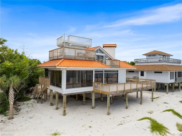 Back of property featuring a balcony, a sunroom, a metal roof, and stairway