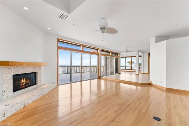 Unfurnished living room featuring ceiling fan, wood finished floors, a tile fireplace, a water view, and a wall of windows