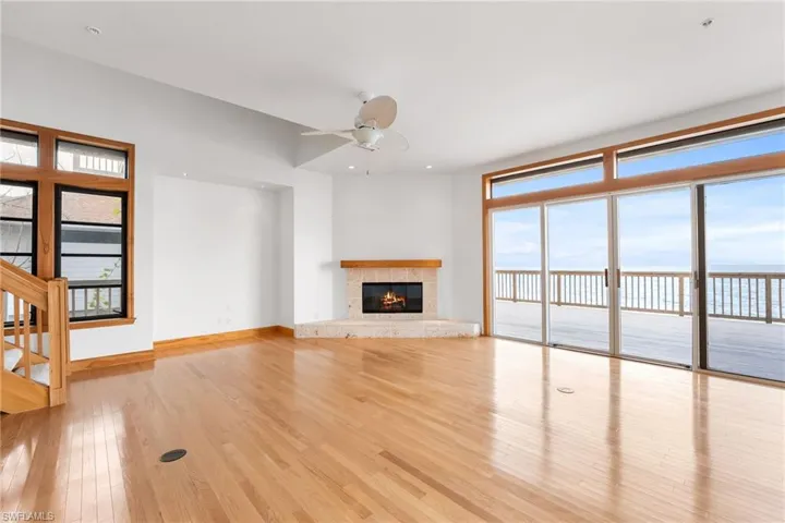 Unfurnished living room featuring a water view, wood finished floors, ceiling fan, a fireplace, and stairs