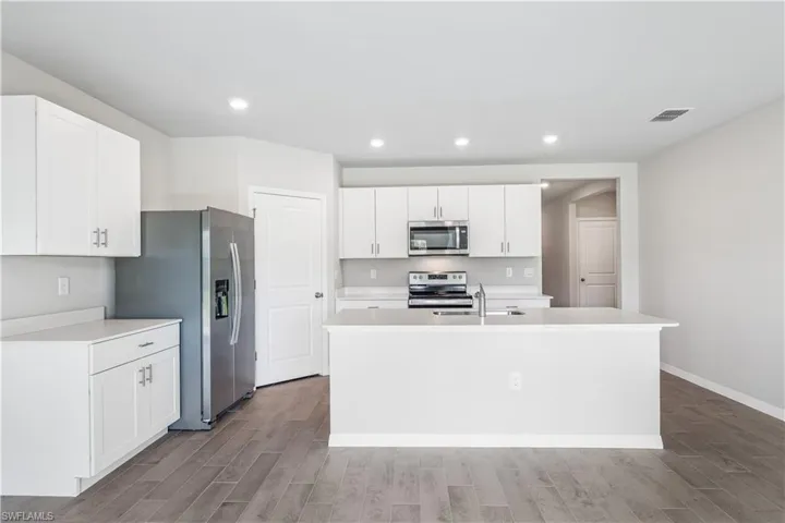 Kitchen featuring appliances with stainless steel finishes, a kitchen island with sink, white cabinets, and light hardwood / wood-style floors