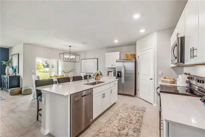 Kitchen with an island with sink, sink, white cabinetry, appliances with stainless steel finishes, and a kitchen bar