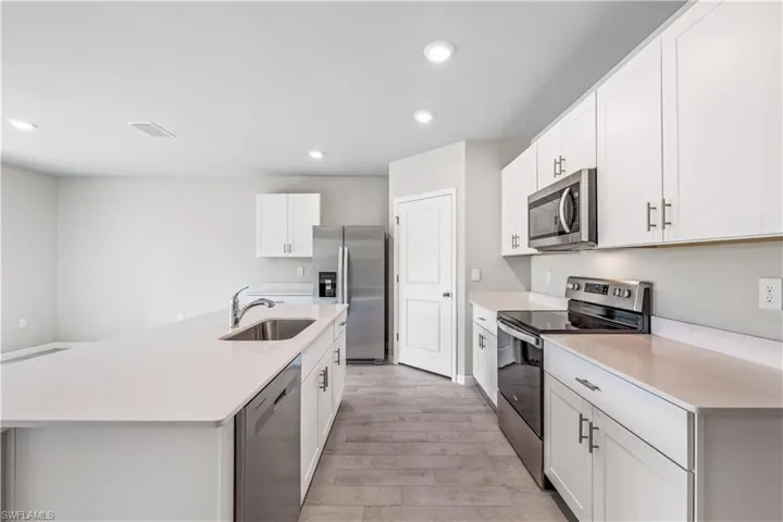 Kitchen featuring a center island with sink, sink, appliances with stainless steel finishes, and white cabinets