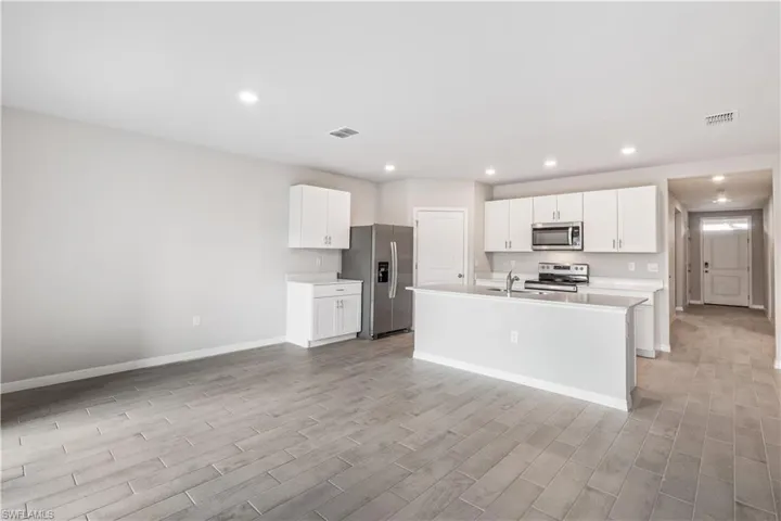 Kitchen with sink, stainless steel appliances, white cabinets, light hardwood / wood-style flooring, and a center island with sink