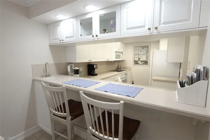 Kitchen with a kitchen bar, white cabinetry, glass insert cabinets, light countertops, and white appliances