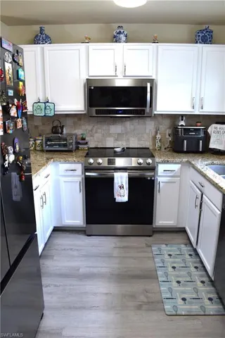 Kitchen with stainless steel appliances, white cabinetry, light stone counters, and tasteful backsplash