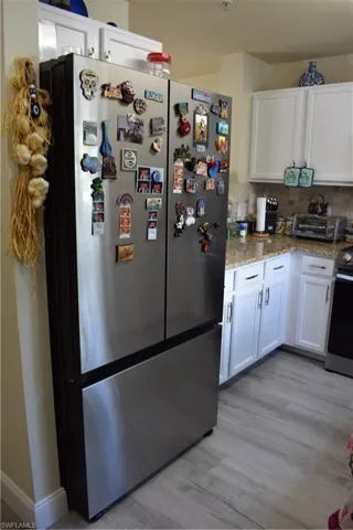 Kitchen with freestanding refrigerator, white cabinetry, range, light stone counters, and backsplash