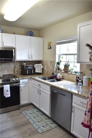 Kitchen with stainless steel appliances, white cabinets, light stone counters, and light wood-style floors