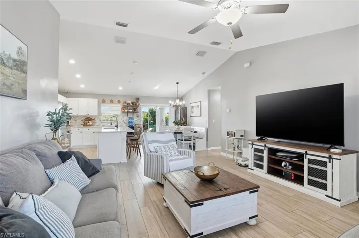 Living room featuring wood finish floors, a chandelier, lofted ceiling, ceiling fan, and recessed lighting